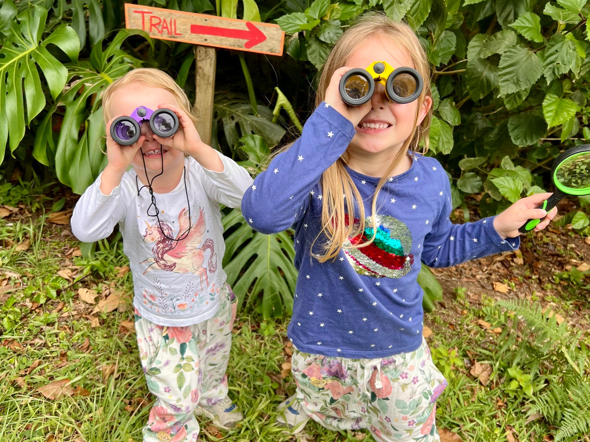 Two young girls are looking through their binoculars at the camera, dressed ready to explore the rainforest